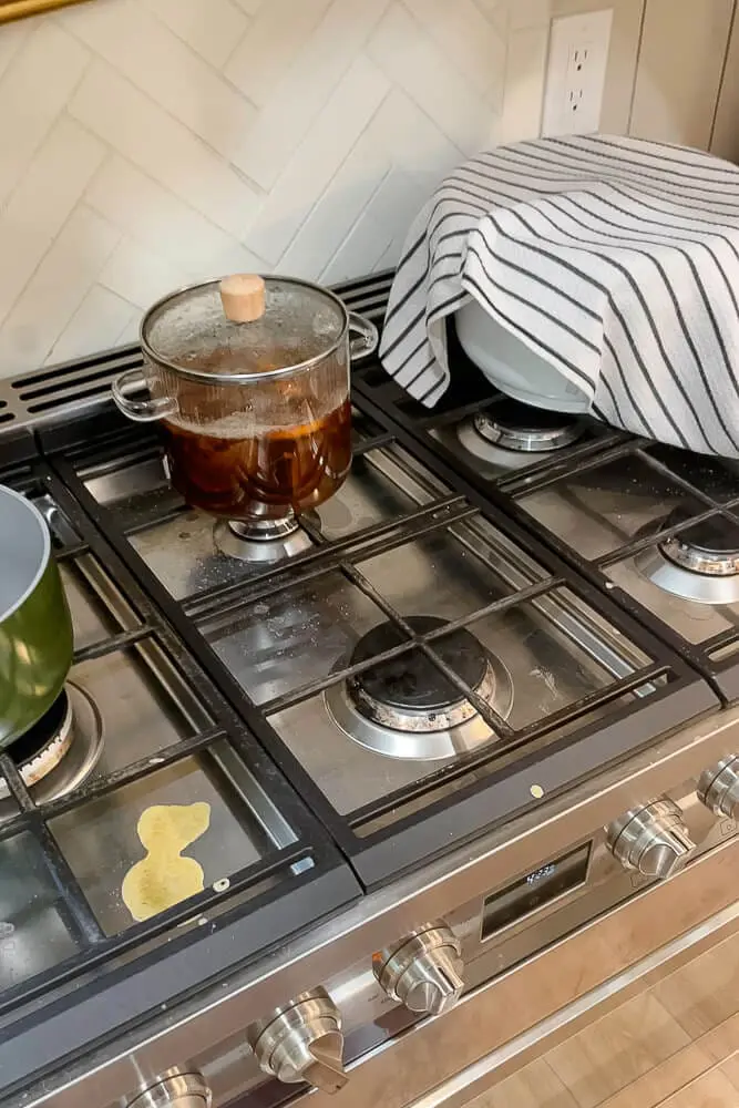 Dough resting under a striped cloth on the stove to rise, a key step in making soft dinner rolls.