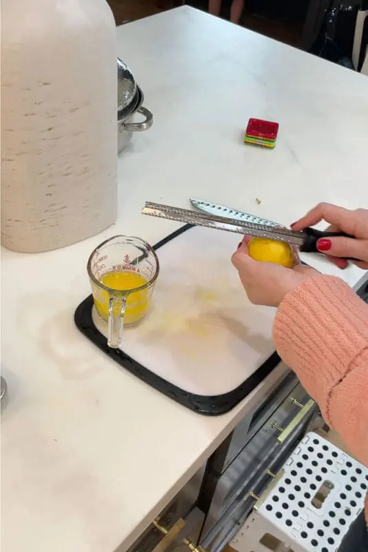 A person zesting a lemon over a measuring cup of melted butter for preparing a super moist and tender turkey.