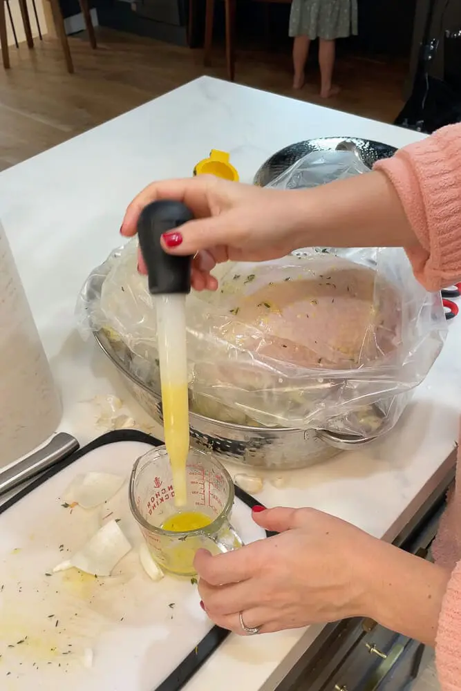 A turkey baster filled with butter being used to baste the turkey inside the roasting bag, ensuring it stays super moist and tender.