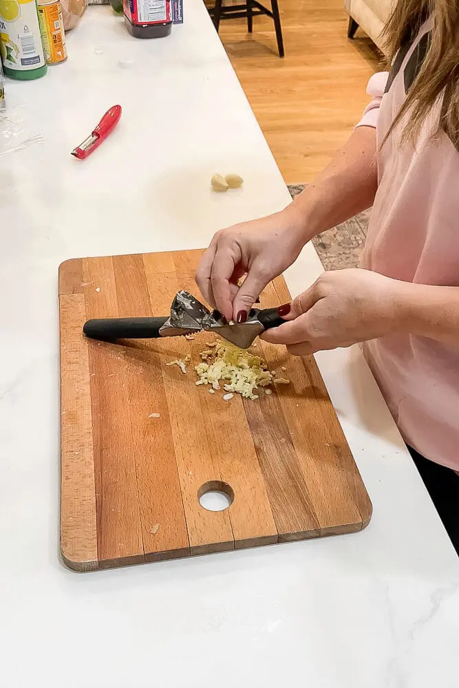 A person mincing fresh garlic on a wooden cutting board, preparing ingredients for garlic mashed potatoes.