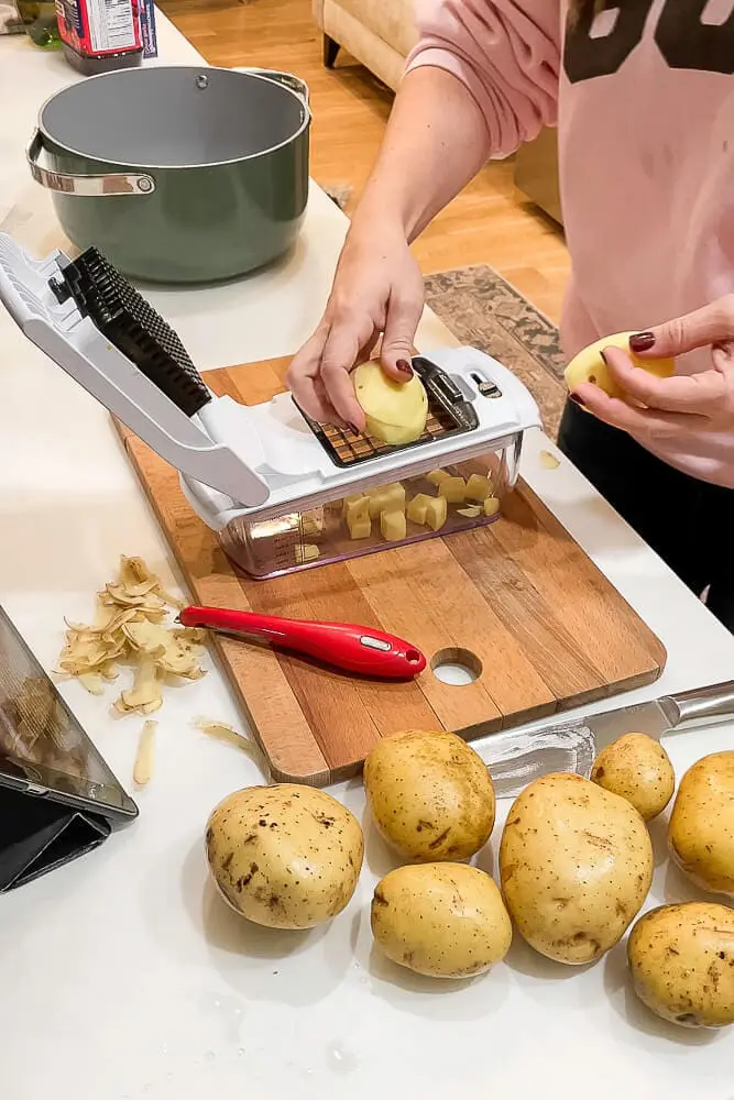A person dicing potatoes with a mandoline slicer on a cutting board, getting ready to cook garlic mashed potatoes.