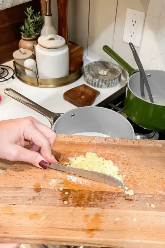 Minced garlic being scraped from a cutting board into a pot, adding flavor to garlic mashed potatoes