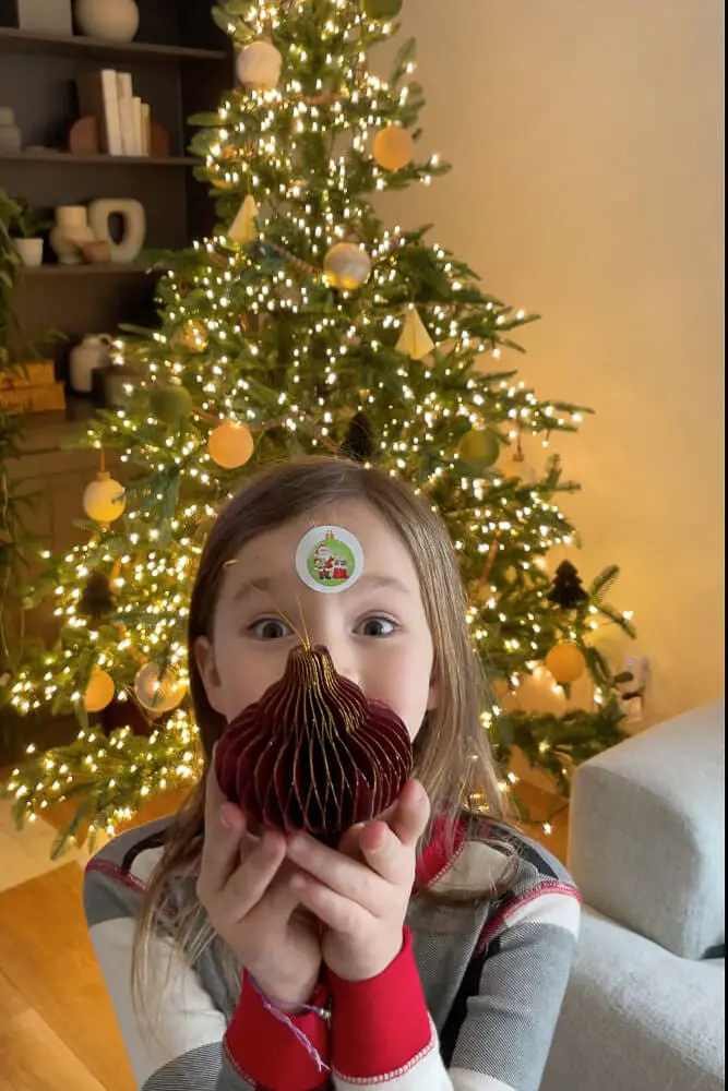 girl holding deep red paper christmas tree ornament