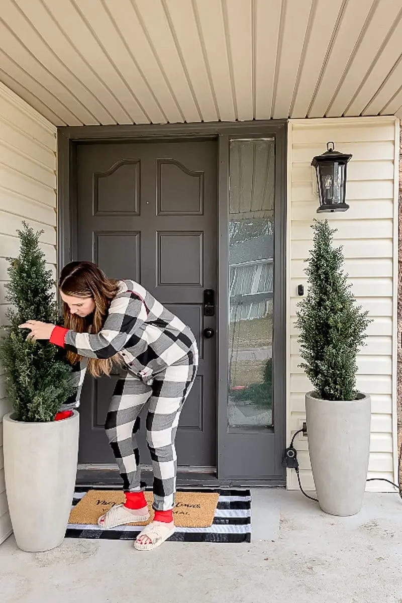 Woman placing faux cedar topiaries in concrete planters on front porch