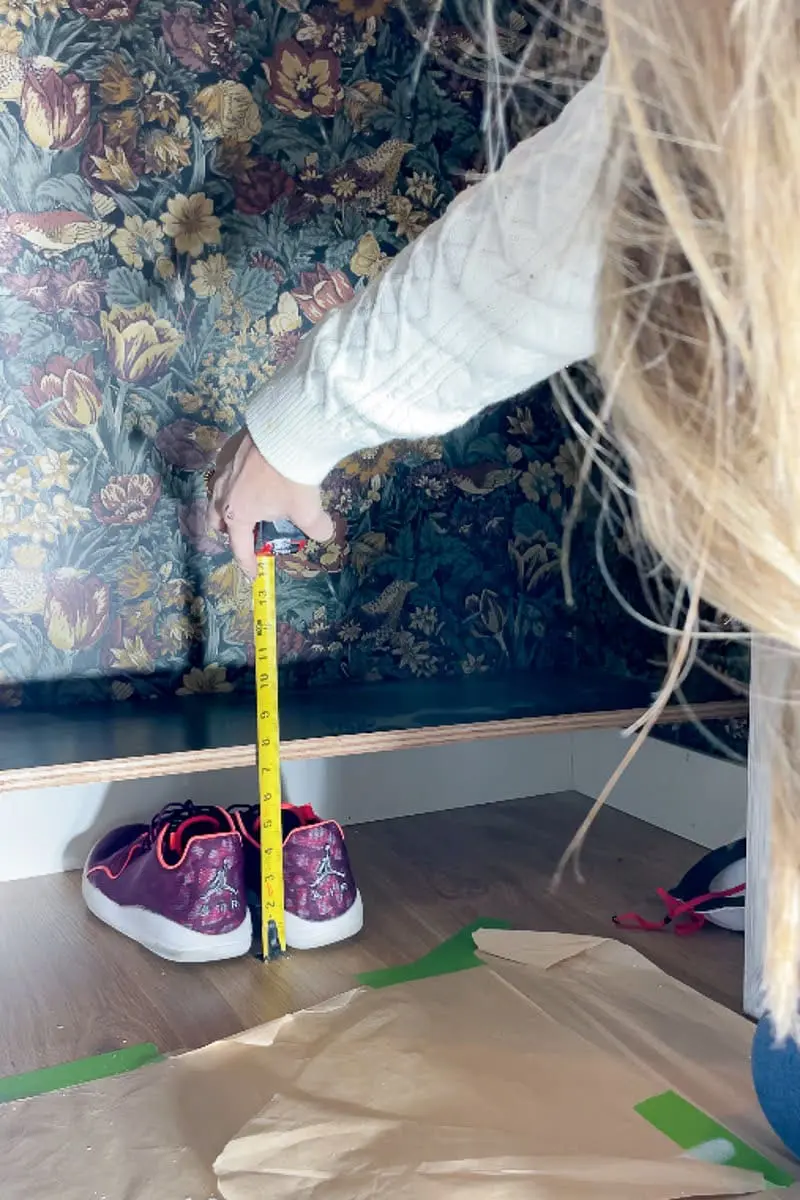 Lady measuring from floor up to where cleat should sit on wall for shelf