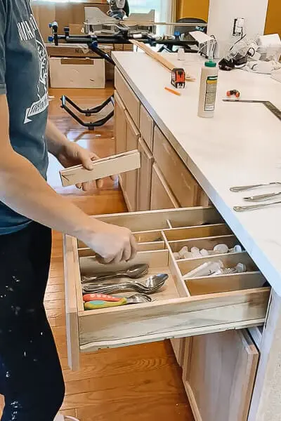 Person cutting plywood pieces to create custom DIY drawer dividers for better organization.
