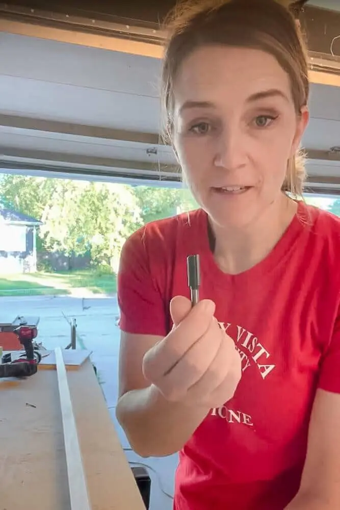 "Close-up of a person holding a 1/2-inch router bit, preparing to carve grooves into the frame for DIY pull-out shelves in a kitchen cabinet.