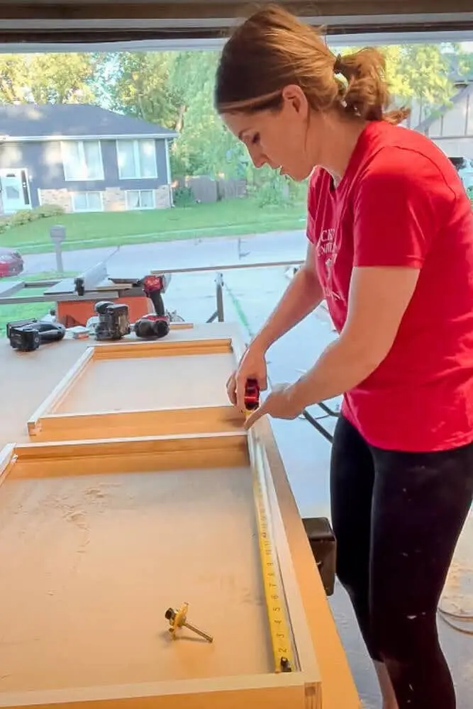 Measuring the width of a kitchen cabinet interior with a tape measure to determine the exact dimensions for DIY pull-out shelves.