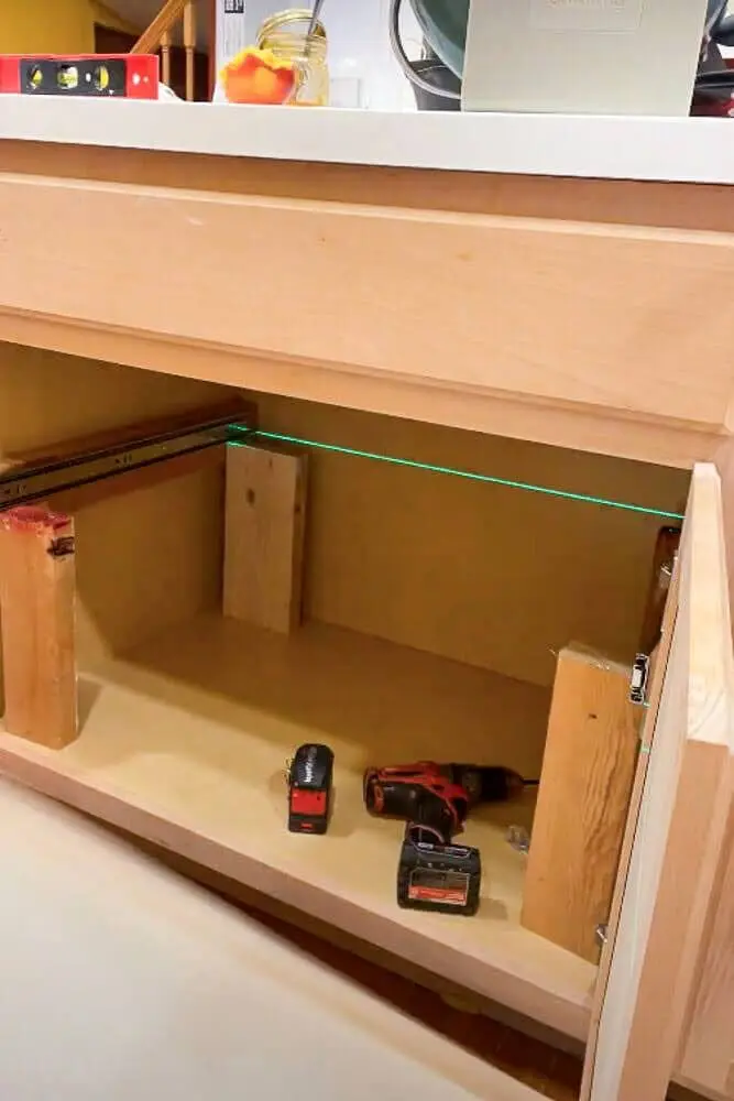 Using a laser level to align and install support blocks inside a kitchen cabinet before mounting 
