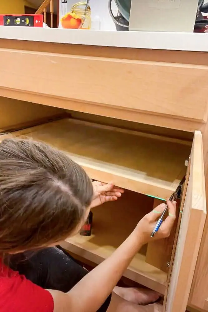 Measuring the front of a kitchen cabinet drawer to mark the placement of the pull-out shelf slides for precise installation.