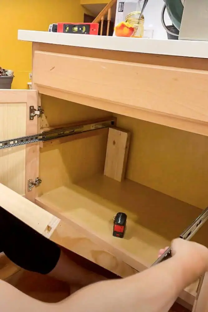 Installing drawer slides on a DIY pull-out shelf, ensuring proper alignment inside the kitchen cabinet for smooth operation.