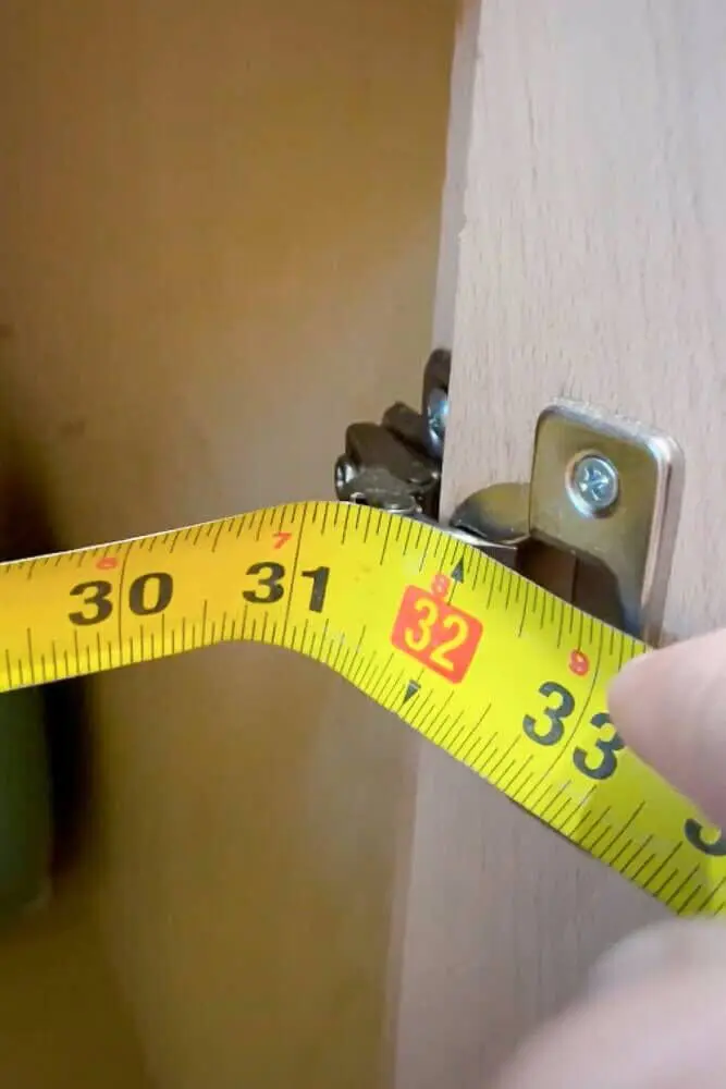 Measuring the inside of a kitchen cabinet from hinge to hinge to determine the correct width
