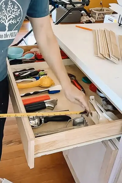 Person measuring the inside of a kitchen drawer to create a custom DIY drawer organizer.