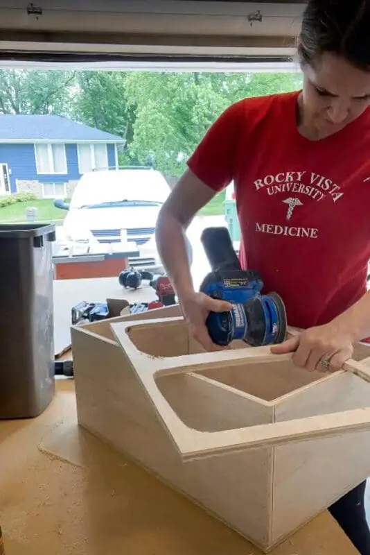 using orbital sander to sand edges of wood box for sliding trash drawer