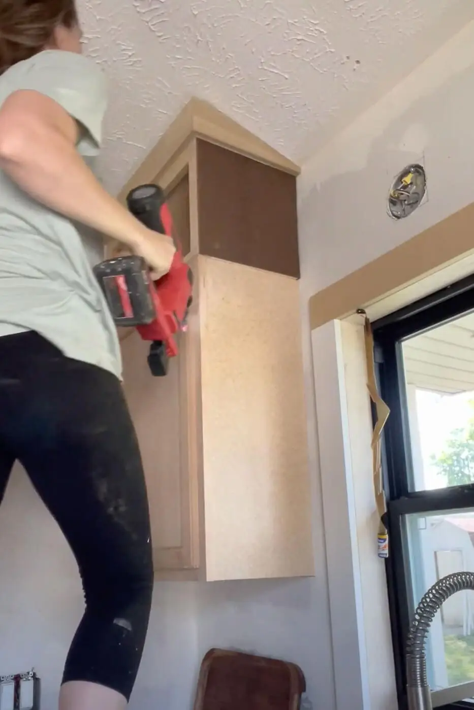 Woman adding crown molding to her kitchen cabinets.