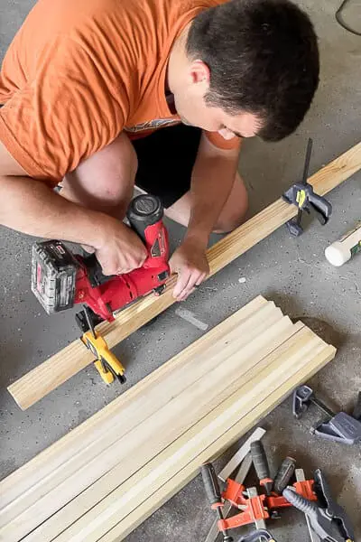 Person using a brad nailer and clamps to attach trim pieces for Murphy bed build
