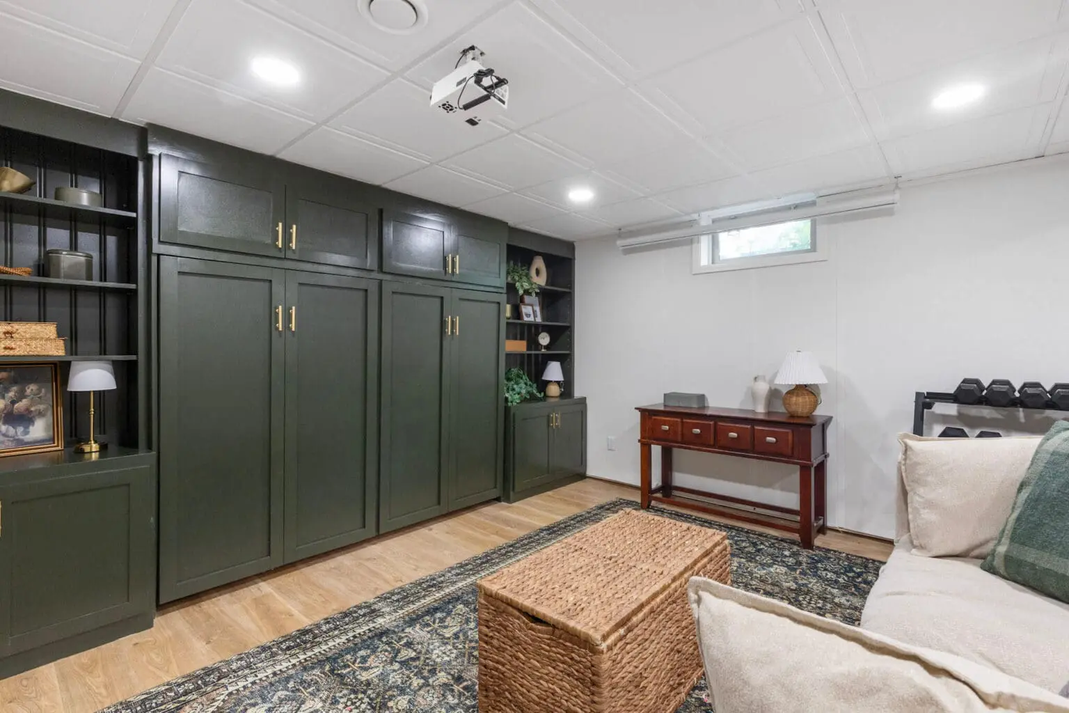 Wall of built-in cabinetry with horizontal Murphy bed closed and fully concealed, blending into green cabinets with brass hardware