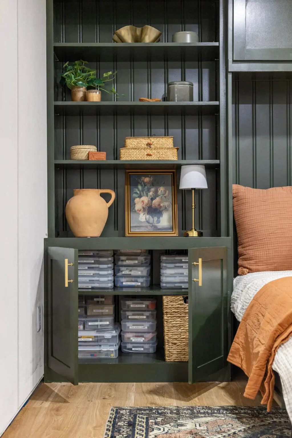 Built-in shelving around horizontal Murphy bed with open cabinet doors showing clear plastic storage boxes and styled decor on upper shelves