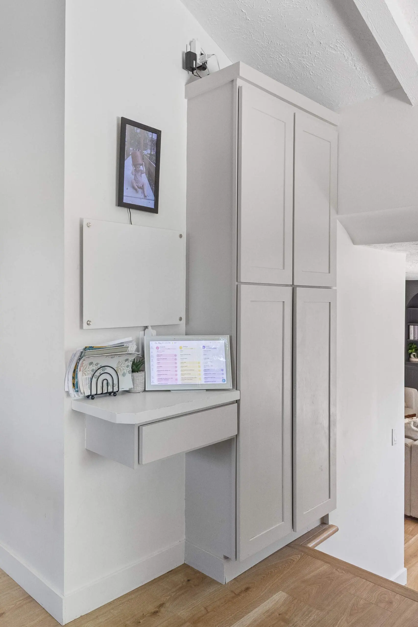 Compact wall-mounted command center featuring a floating desk, digital family schedule, wall organizer, and paper sorter next to tall built-in cabinetry.