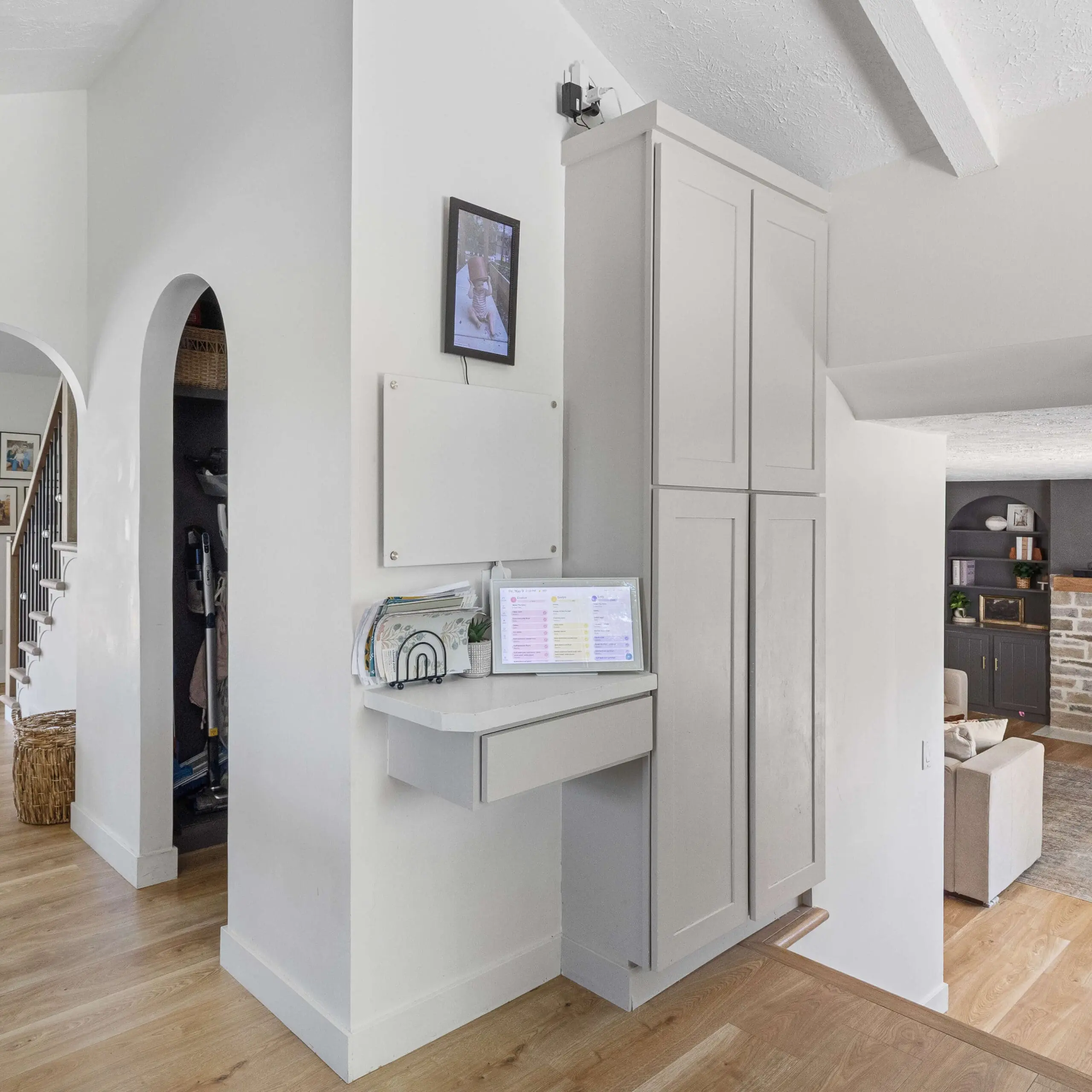 Modern wall-mounted family command center with a floating desk, paper organizer, and digital calendar setup tucked between a hallway and kitchen cabinetry.