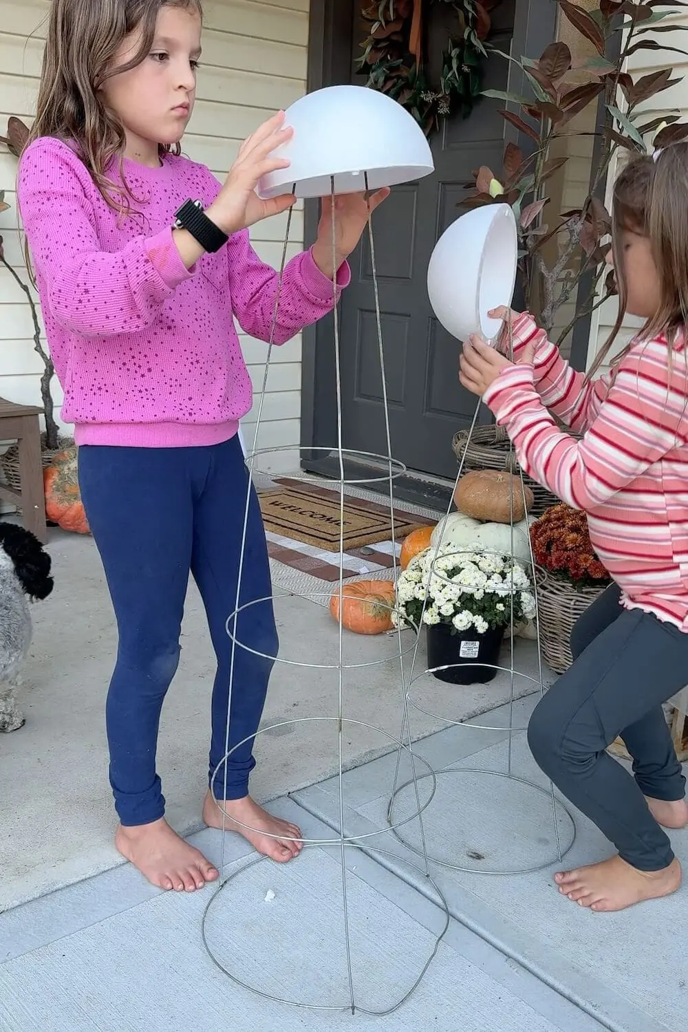 Kids building tall sheet ghost frames with tomato cages and foam domes by the front door.