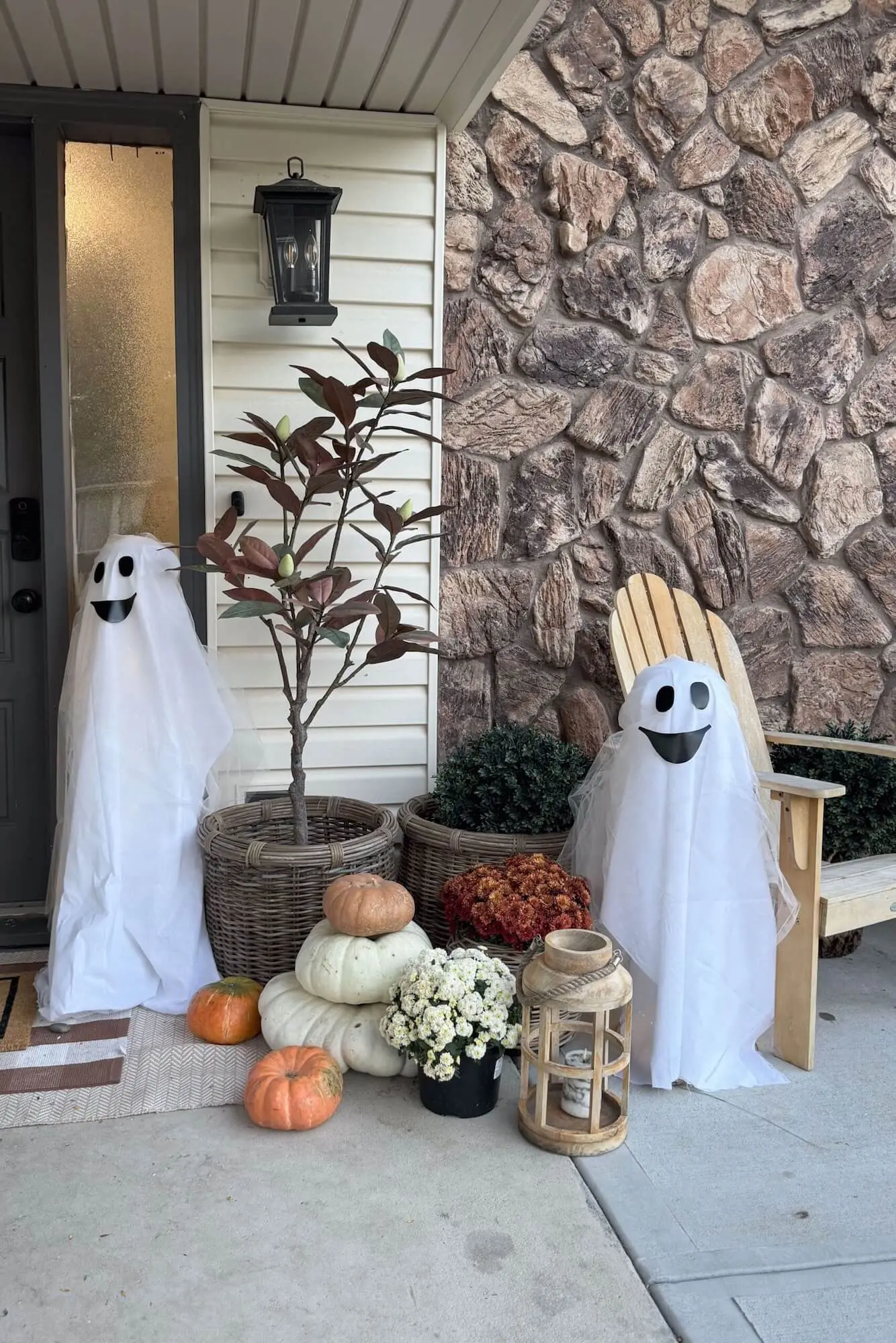 Daytime porch with three DIY glowing sheet ghosts, pumpkins, mums, and a layered doormat.