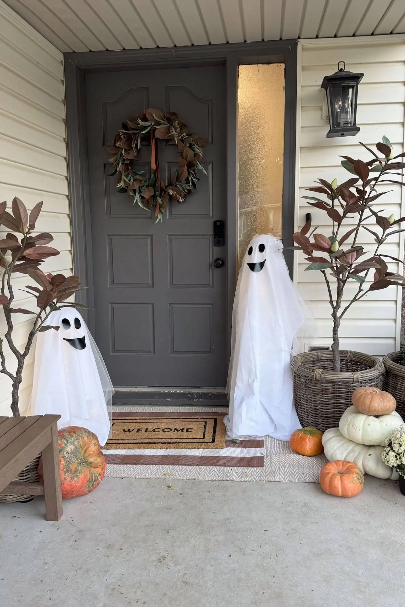 Two porch ghost decorations flanking the gray front door with pumpkins and wicker planters.
