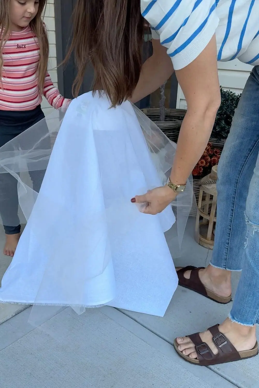 Draping white fabric and tulle over a ghost frame while a child helps on the porch.