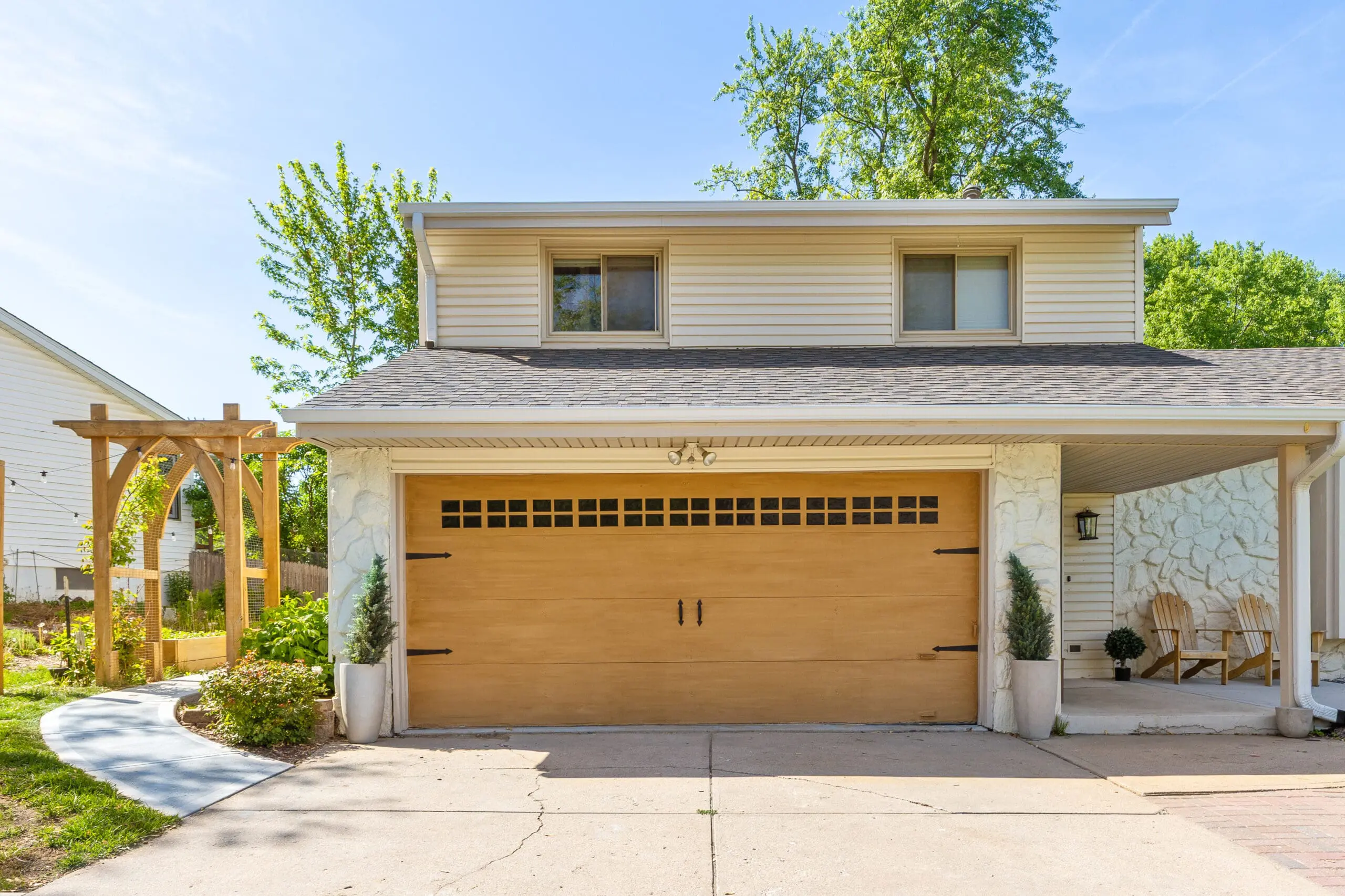 Clean front exterior view showcasing a DIY faux wood garage door, neutral stone facade, and a curved sidewalk leading to a wooden garden arbor.