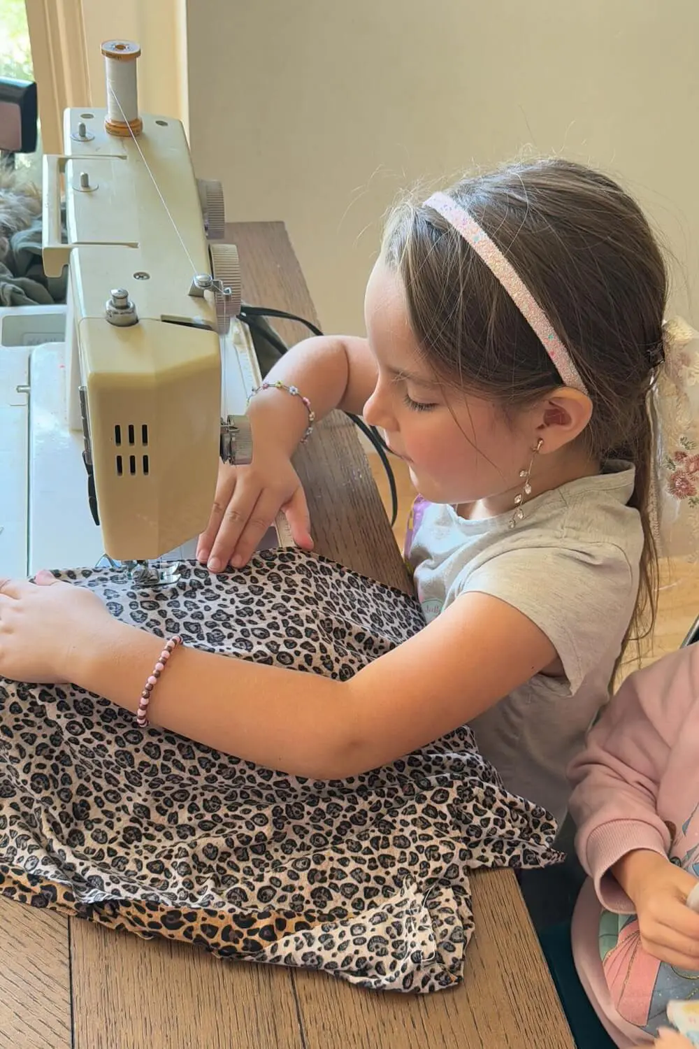 Girl sewing leopard-print fabric on a home sewing machine for a costume.