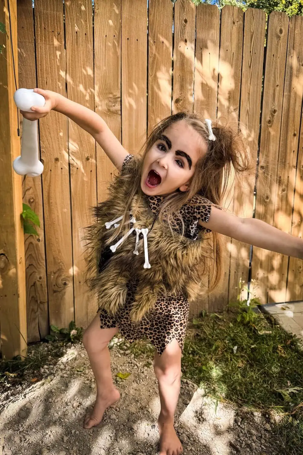 Kid in DIY caveman costume roaring with bone prop and fur vest