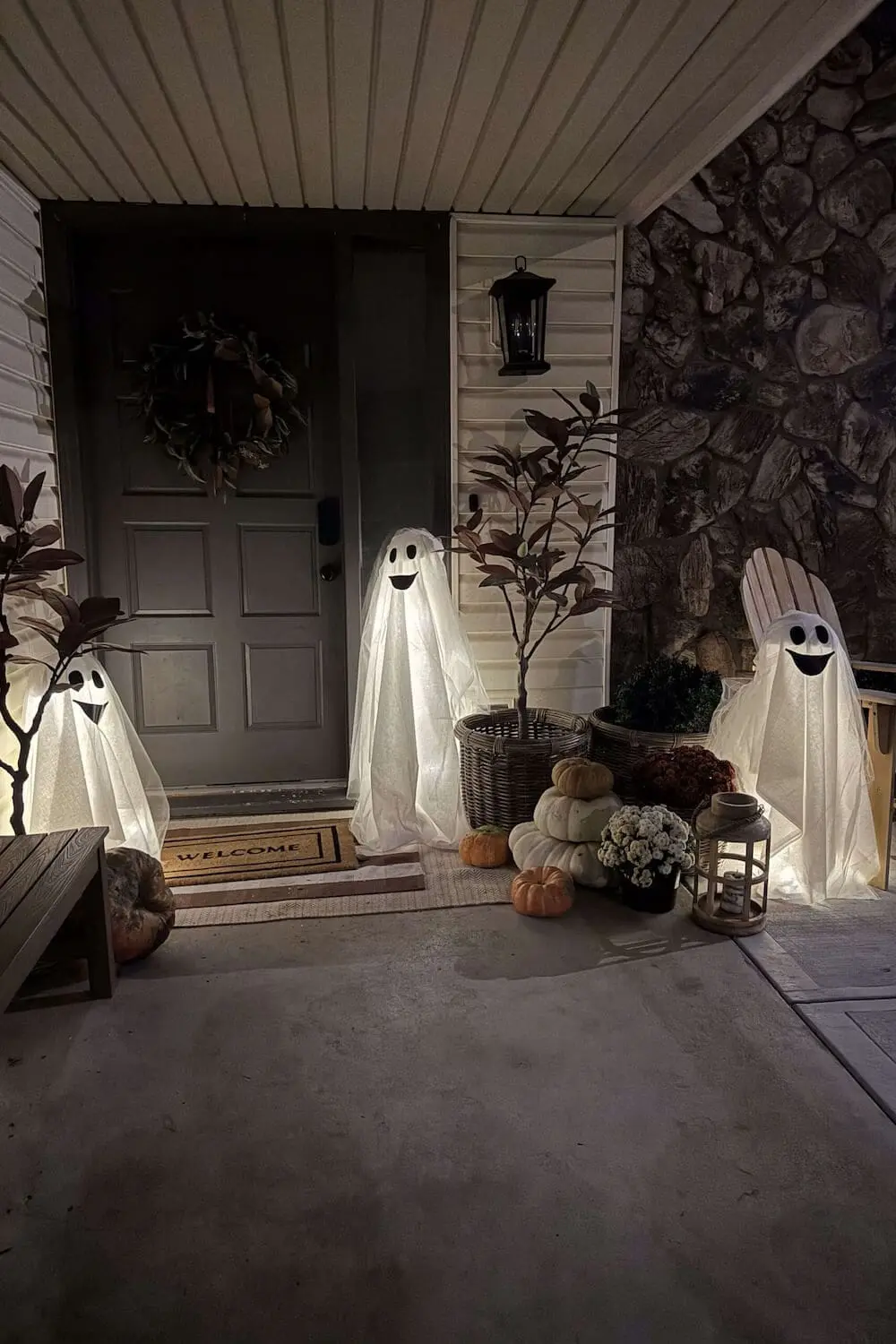 Front porch light-up ghost decorations with pumpkins and lantern at night