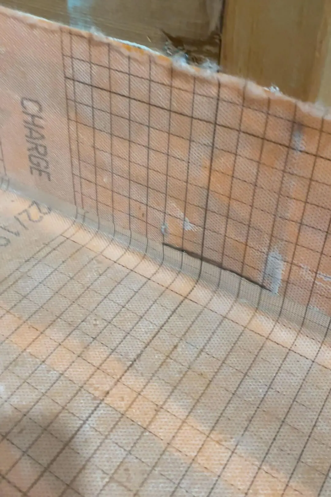 Detailed view of an orange waterproofing membrane on the bathroom floor and lower wall, displaying a grid pattern for precise tile placement. The membrane wraps up the wall slightly, ensuring a watertight seal in this area under construction.