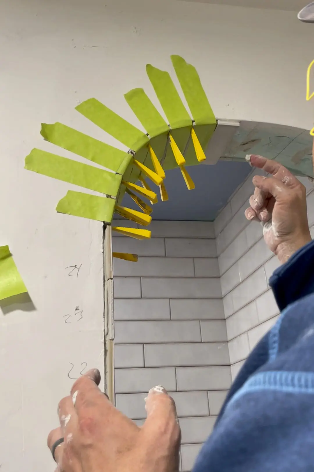 A tiled archway in progress, supported by bright yellow clips and green painter's tape, showcasing meticulous tile installation on the curved surface.