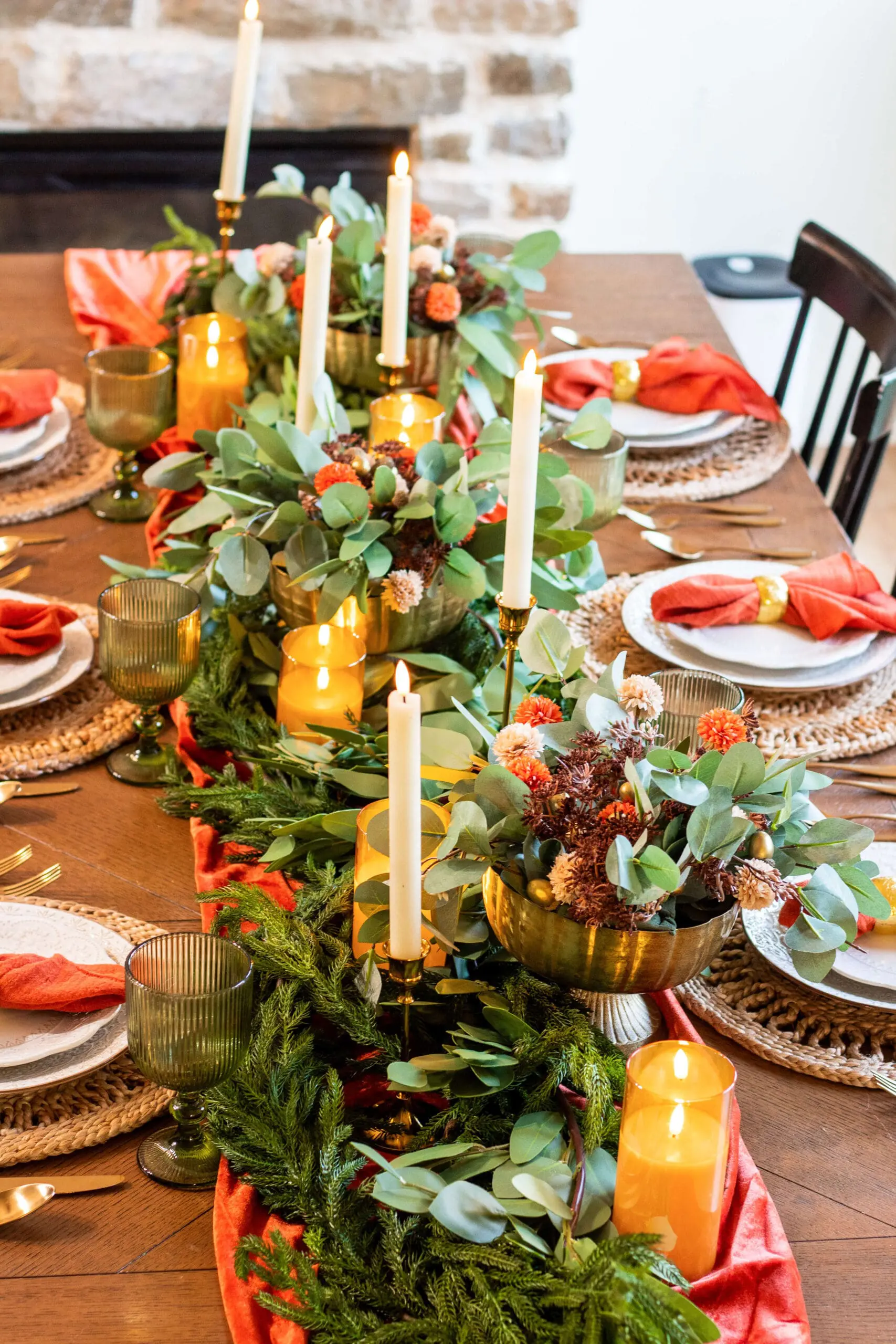 Thanksgiving table decor showcasing a lush centerpiece of eucalyptus, green glassware, orange velvet runner, and warm candlelight for a cozy holiday dinner setup.
