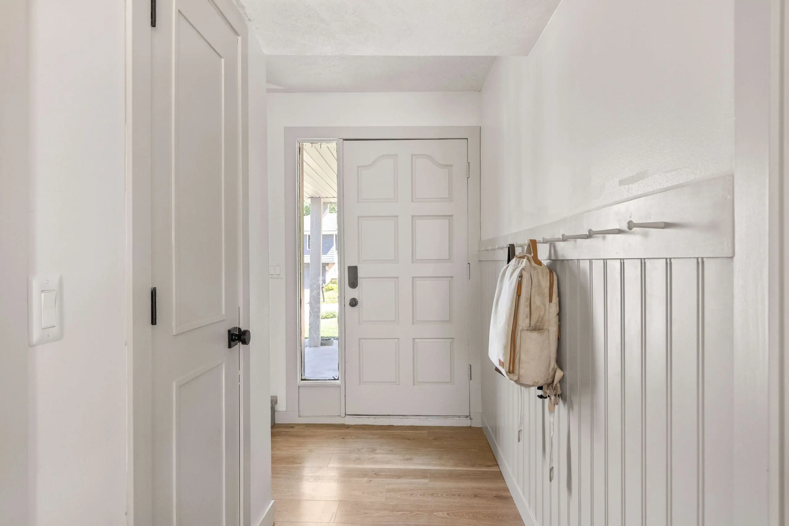 Bright and functional foyer with wall-mounted pegs, neutral tones, and wood floors—designed for quick-drop backpack storage and everyday organization.