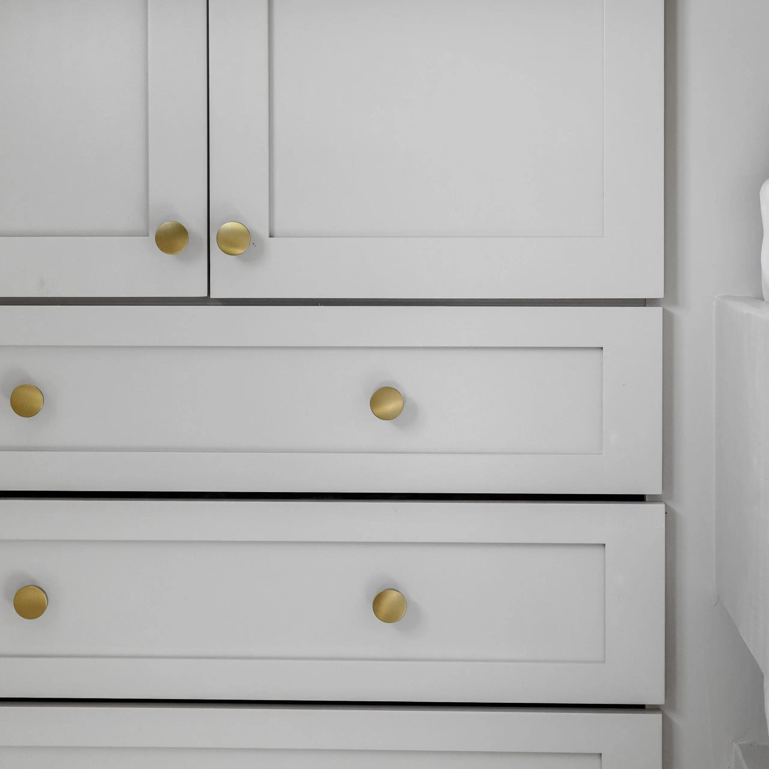 A close-up view of DIY painted white shaker-style cabinets and drawers, featuring modern matte gold round knobs for a sleek and elegant finish, showcasing a clean and minimalistic design.