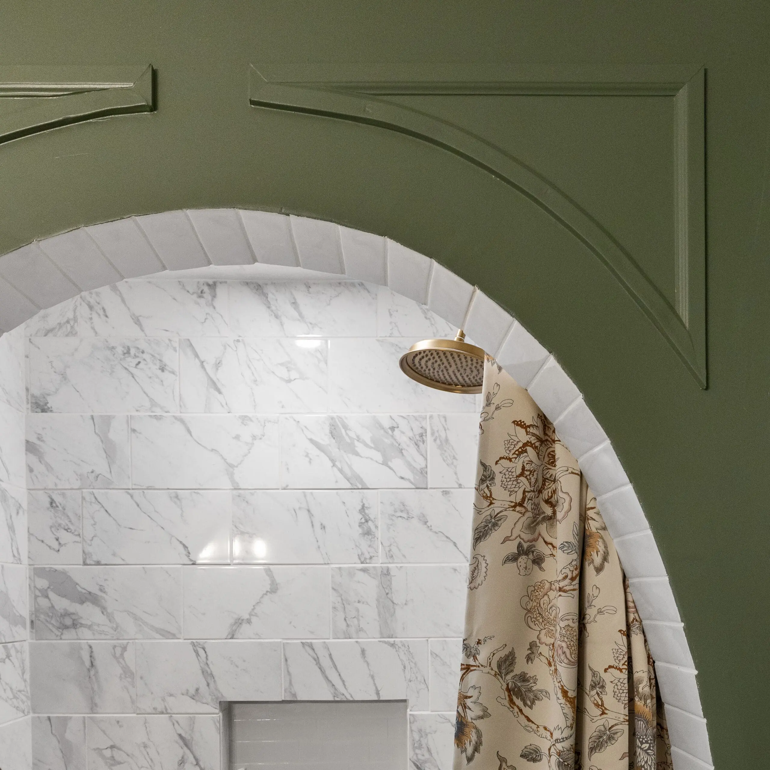 Elegant shower featuring a green arched frame, polished marble tile walls, and a vintage-style brass showerhead with a patterned shower curtain.