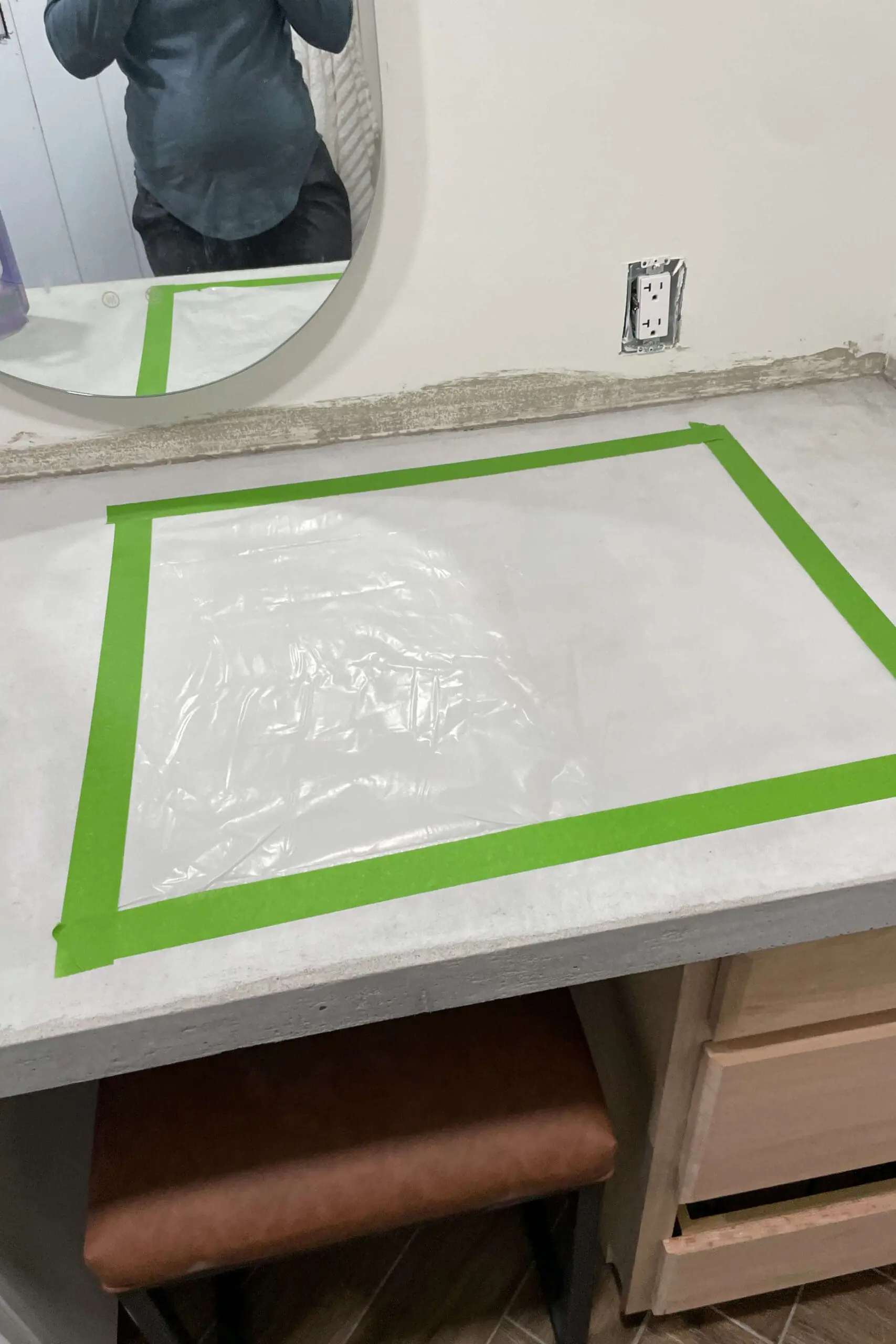 Completed concrete countertop with taped-off sections for a vapor test. Green painter's tape outlines a rectangular area on the surface, and an oval mirror hangs on the wall above.