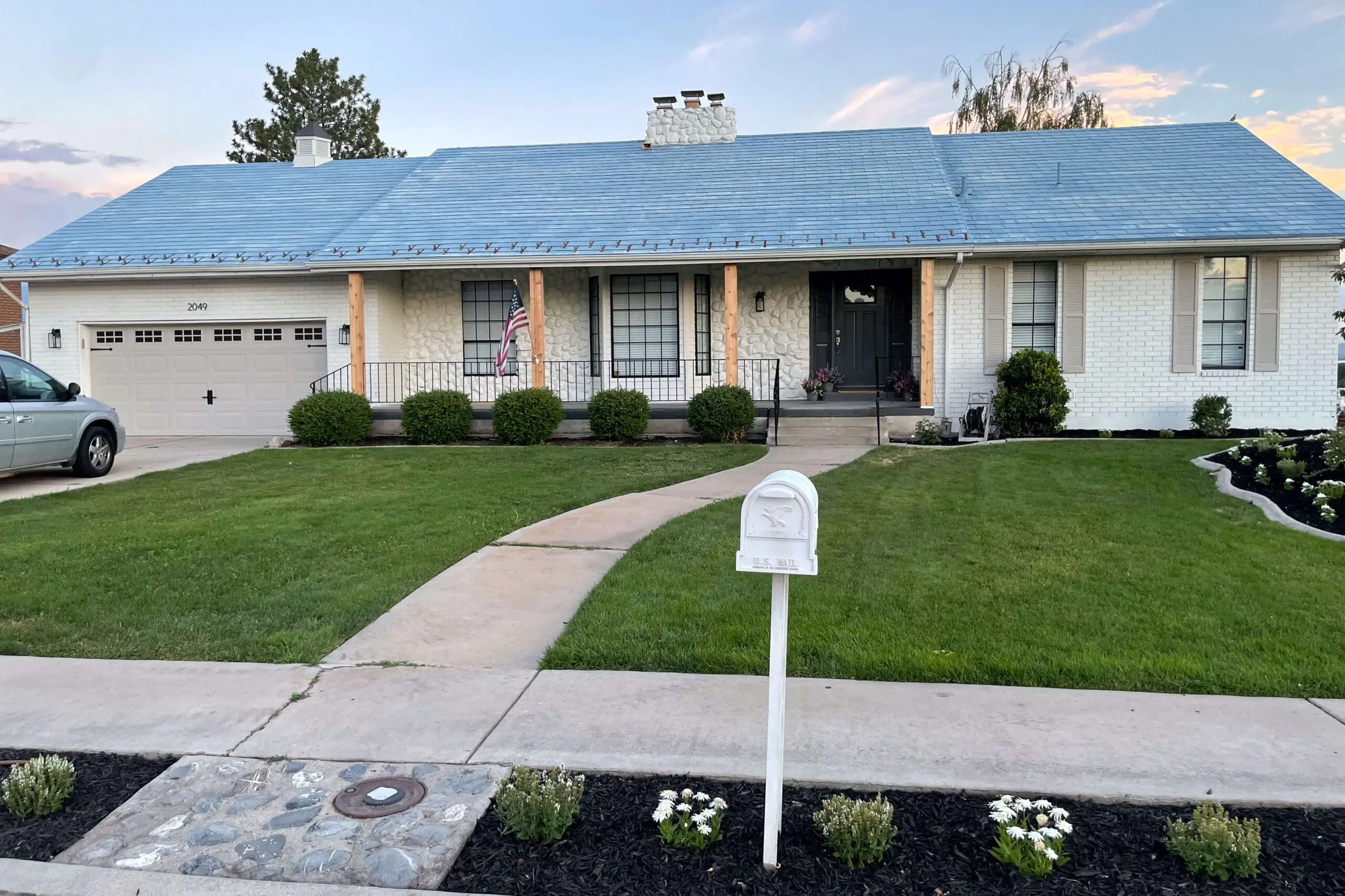 Full front view of a white painted brick home with natural wood porch column wraps, black iron railing, and a curved concrete walkway leading to the front door, adding warmth and character to the classic facade.

