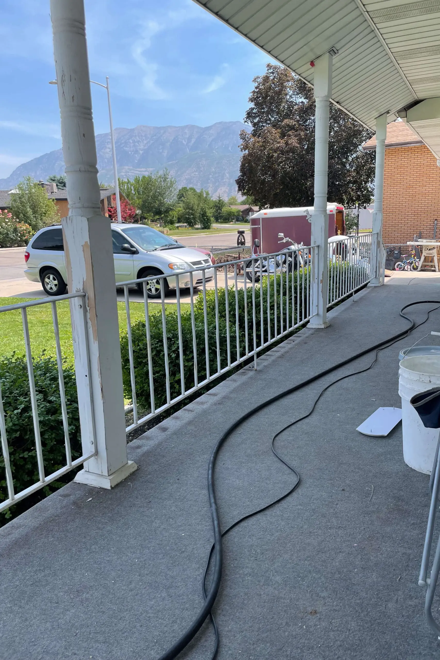 Close-up of worn white metal porch railings and peeling posts before a DIY exterior makeover, with tools and prep materials visible.
