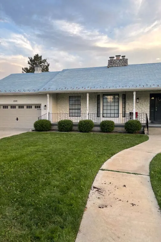 Wide shot of a home’s front porch before a DIY makeover, featuring original decorative columns, black metal railings, and an untouched concrete walkway.