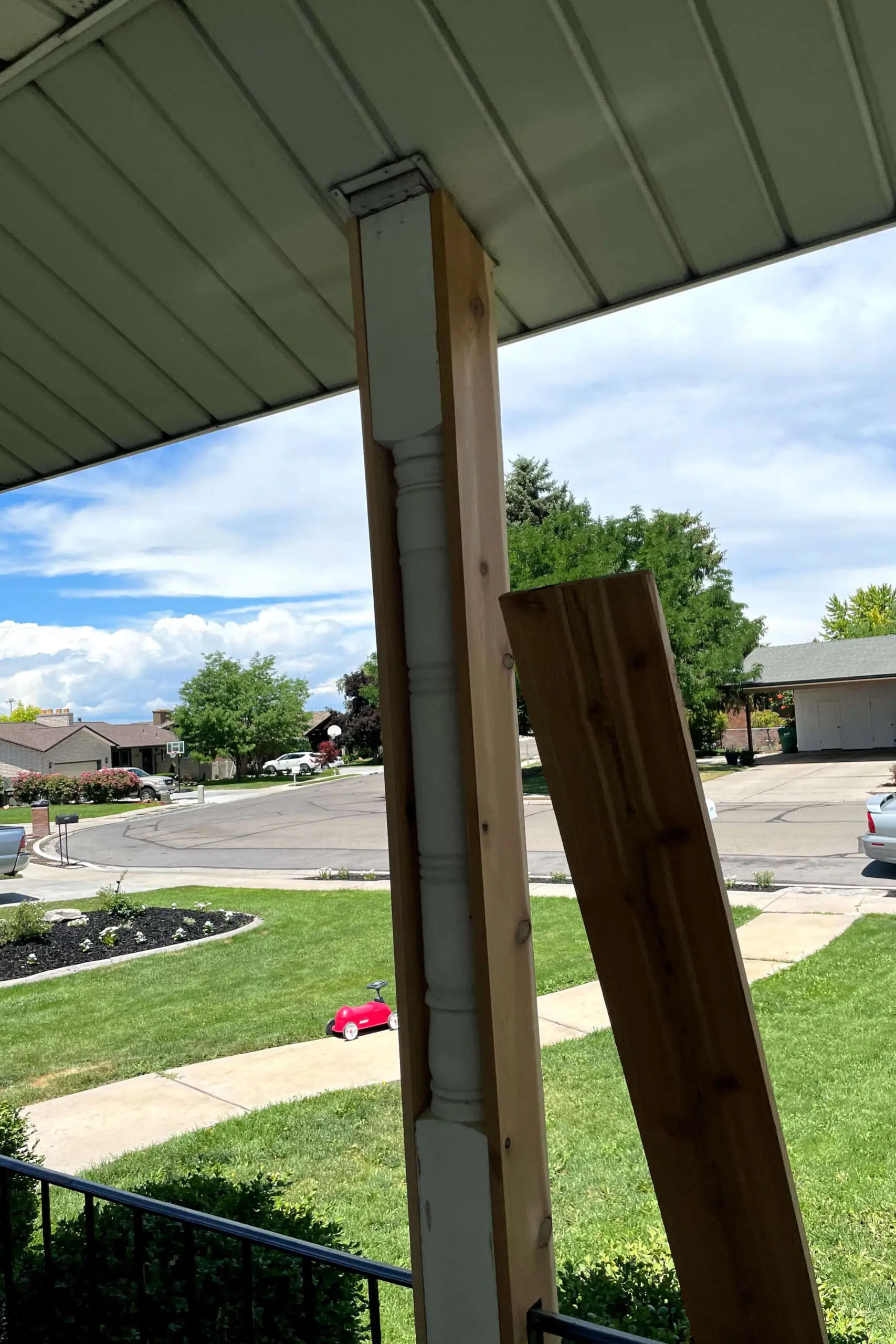 A wooden wrap partially installed around an old porch post with decorative trim, showing the clean-lined cedar boards being fitted for a front porch upgrade.

