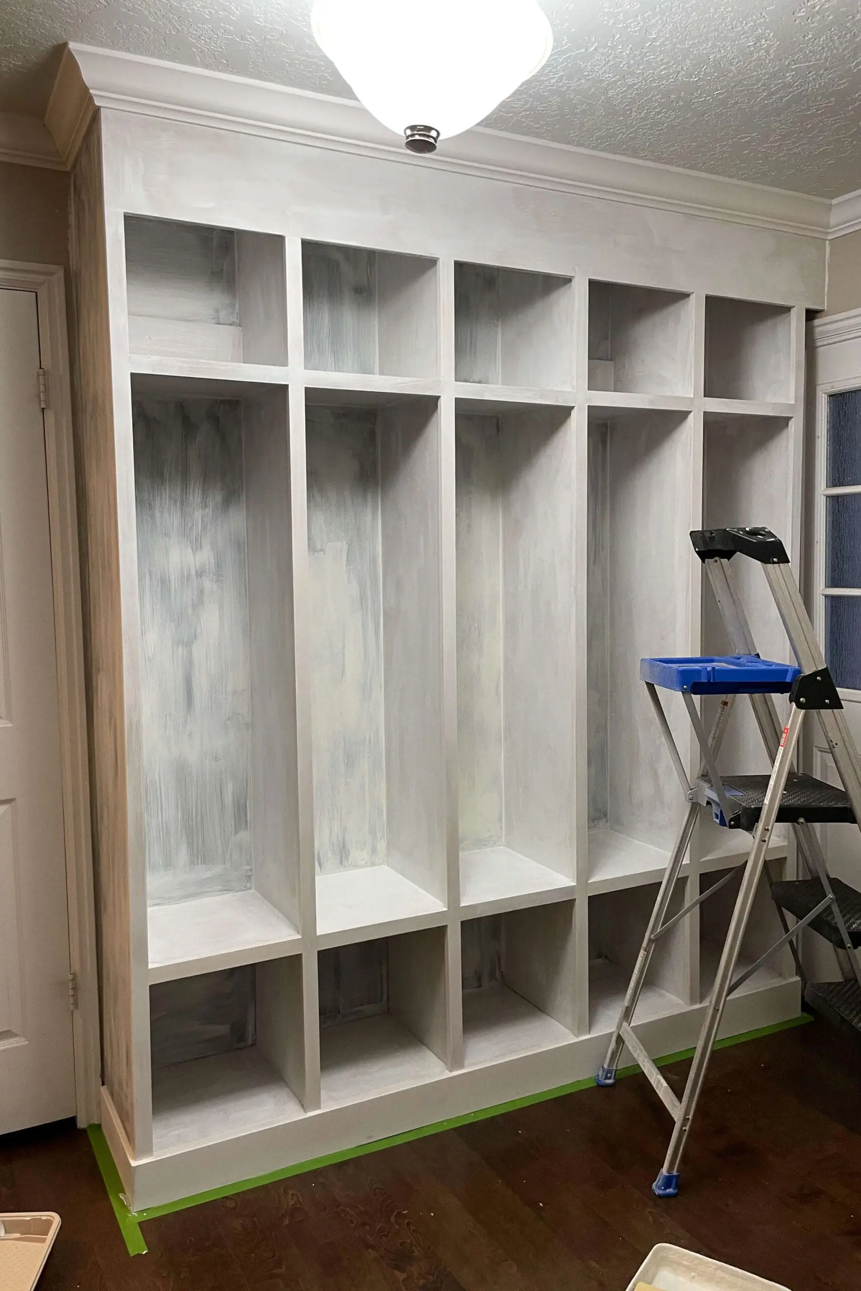 Custom-built mudroom lockers fully primed and ready for final coats of paint, with a step ladder positioned for upper section detailing.