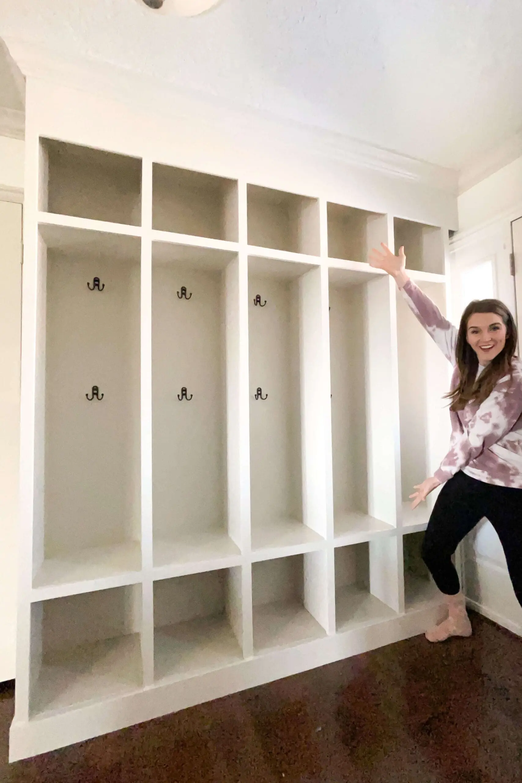 Custom built-in mudroom storage lockers with six tall cubbies, hooks for hanging coats, and open shelving for baskets and shoes.