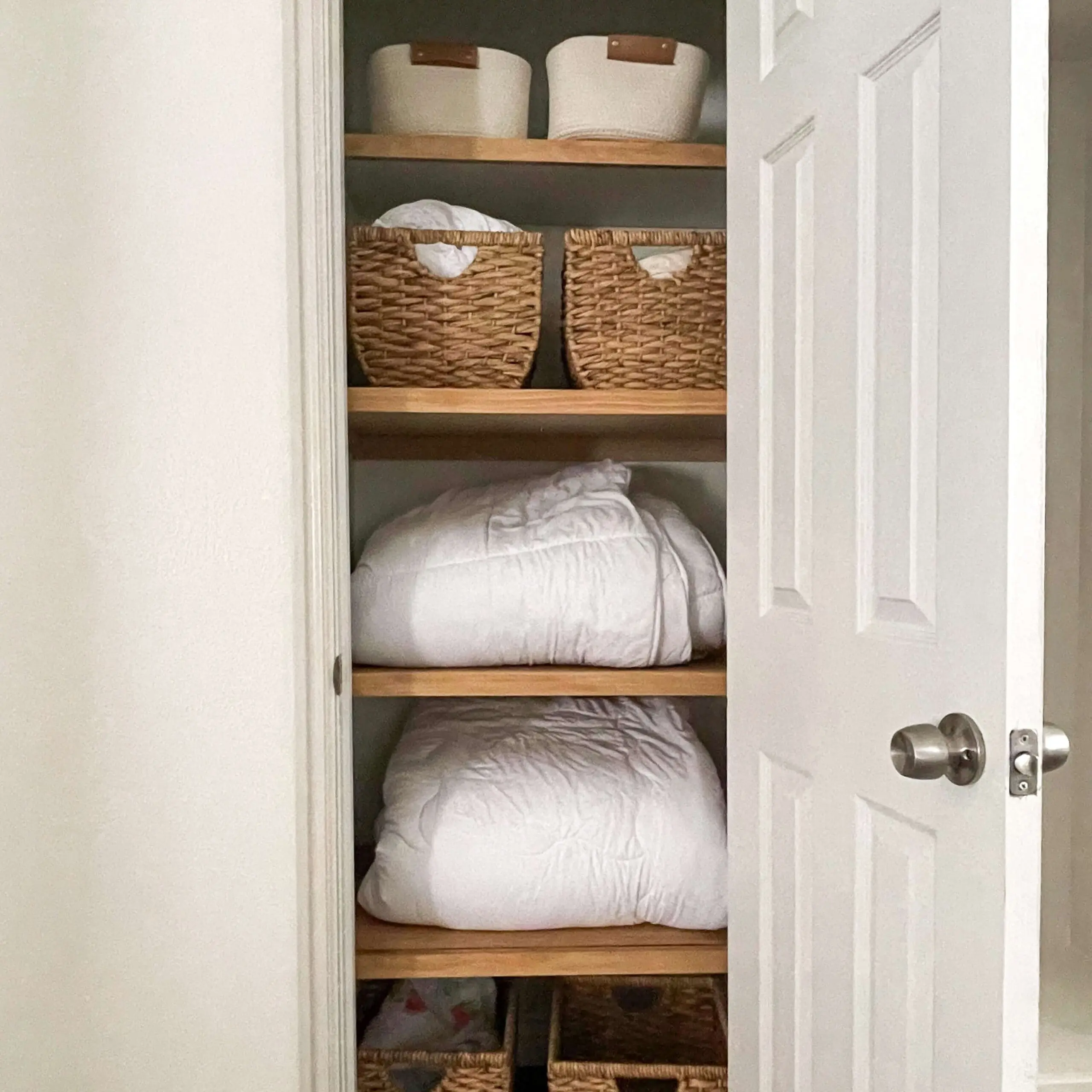 Small closet transformed into a storage-friendly linen closet with DIY closet shelves, woven baskets, and neatly arranged bedding.
