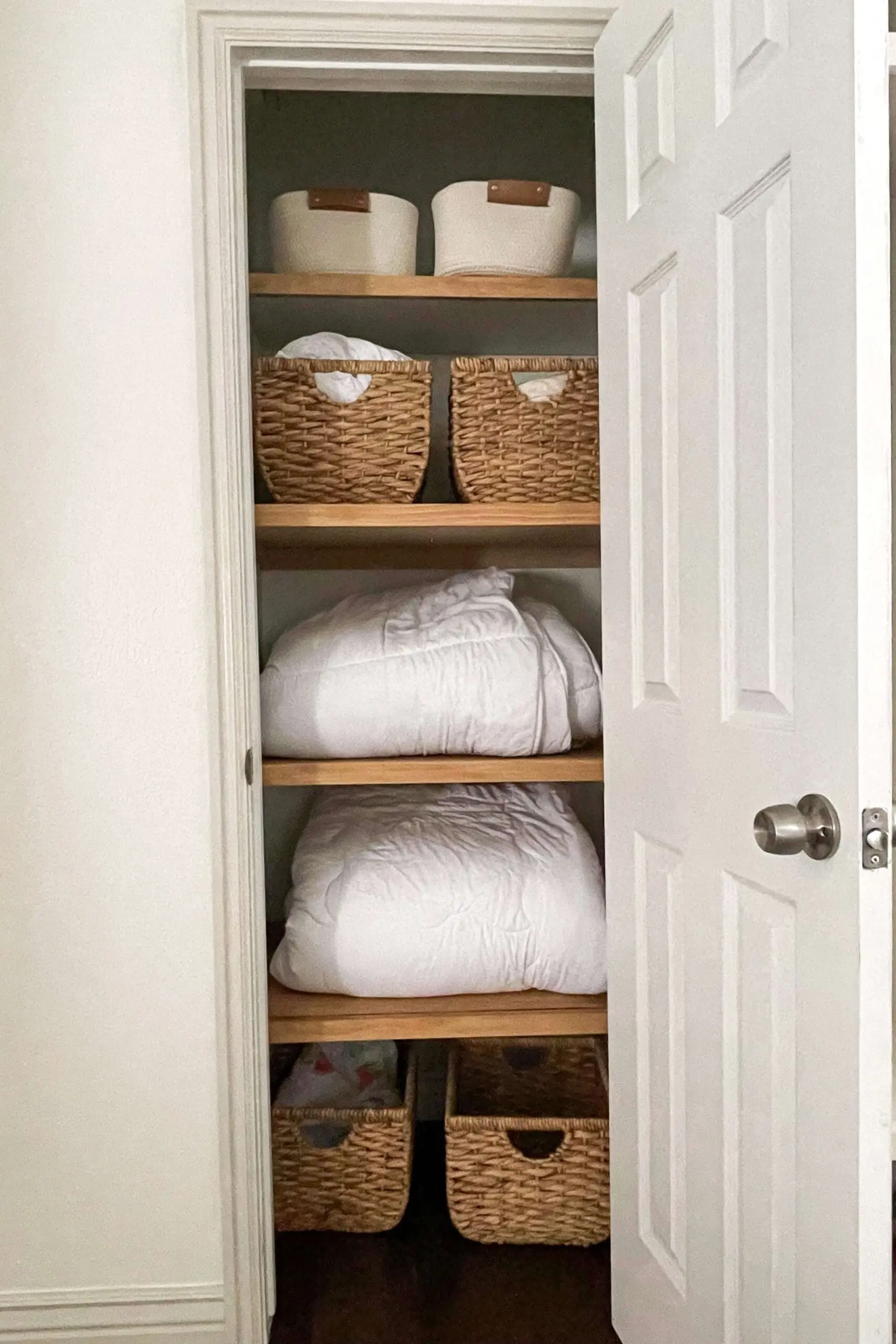 Fully organized linen closet with woven baskets and neatly folded blankets on DIY closet shelves, showcasing a stylish and functional storage solution.