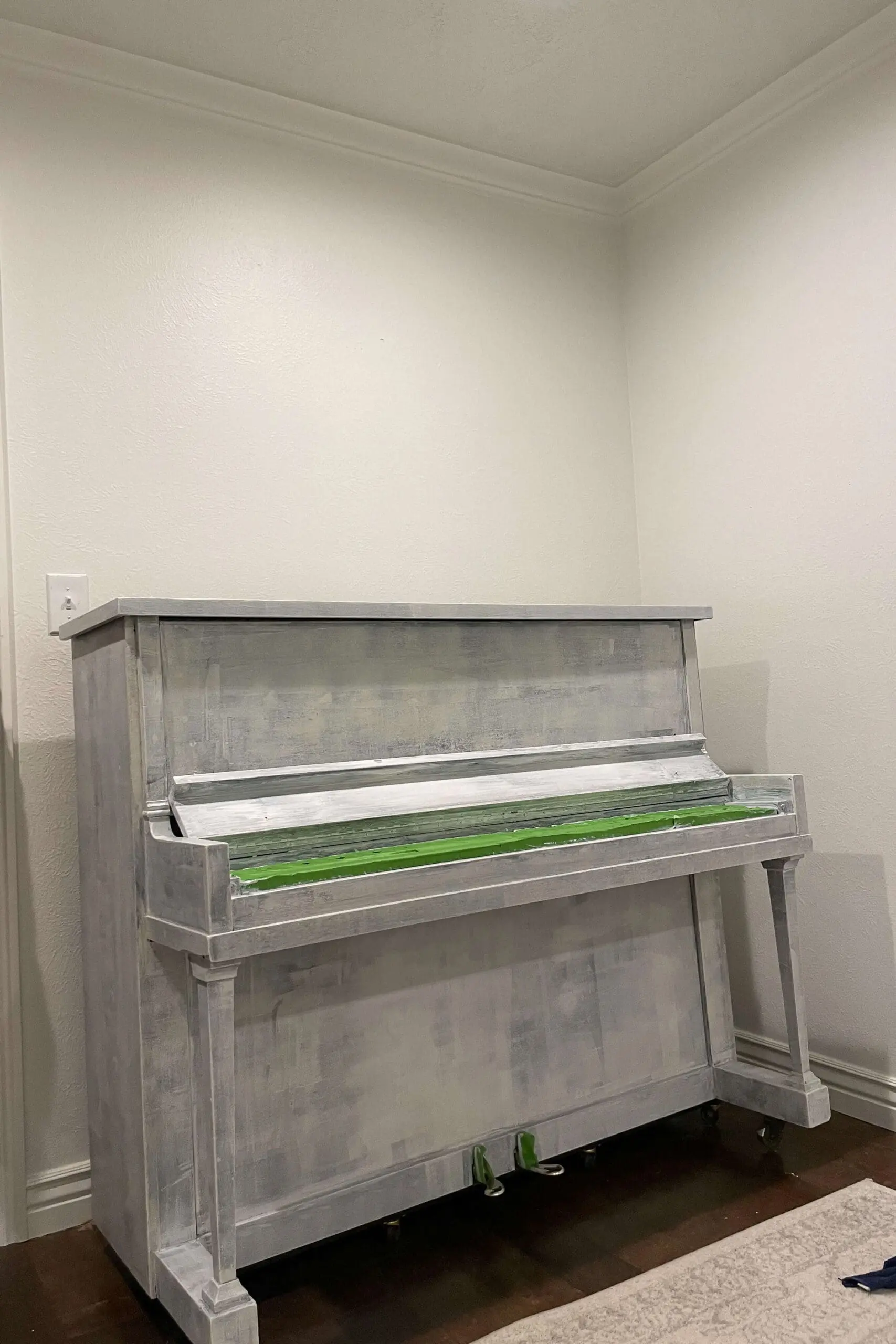An upright piano fully coated in white primer, with painter’s tape applied to protect the keys and pedals before painting.