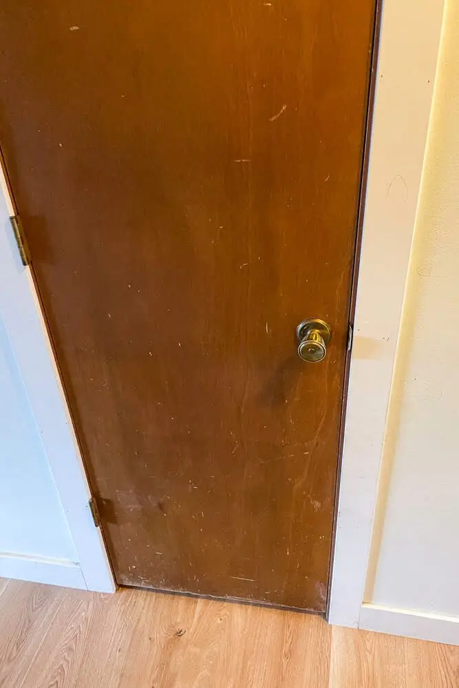 Old wooden door with visible scratches, scuffs, and a brass doorknob, before a DIY makeover and home improvement project.