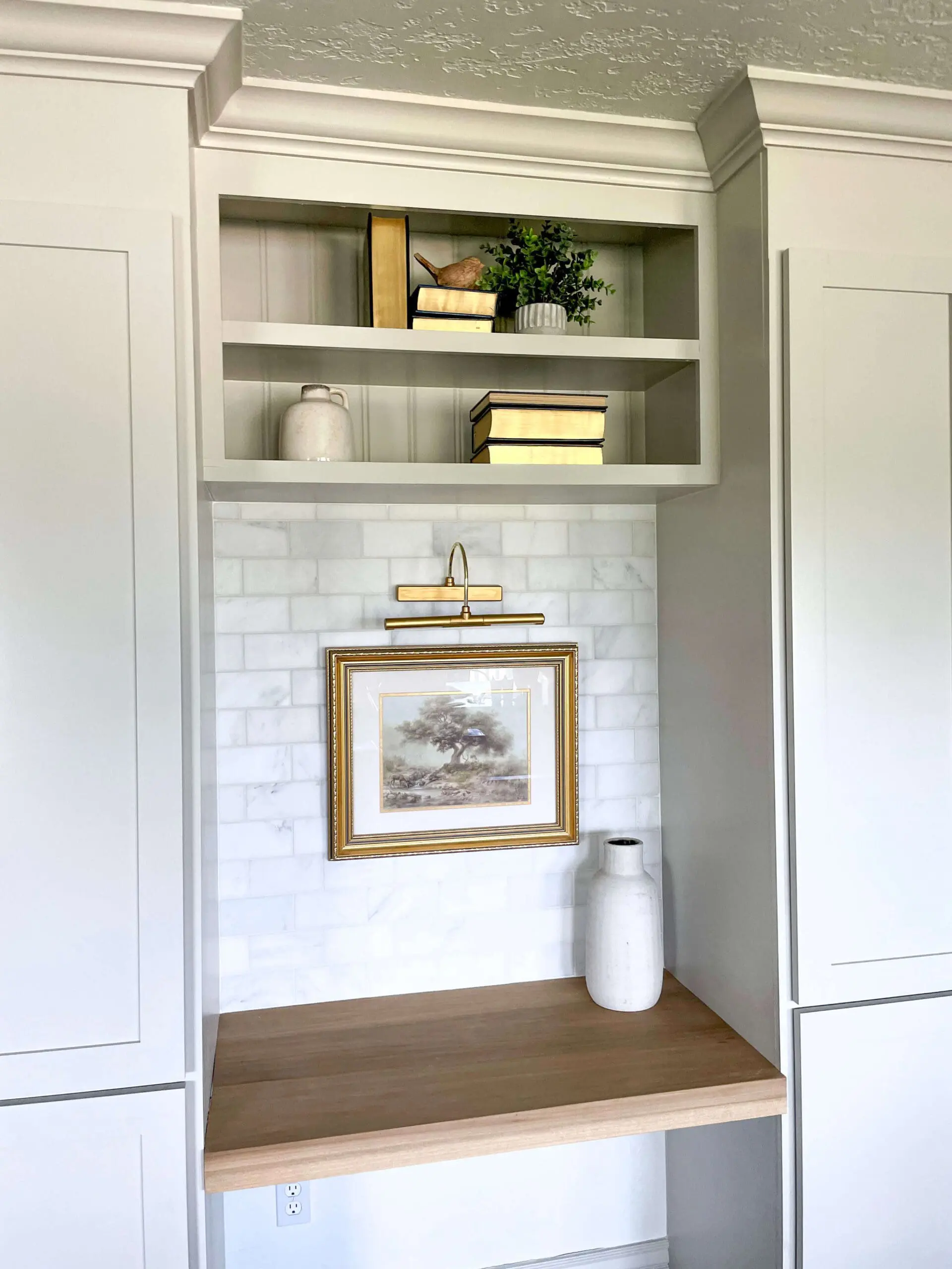 Symmetrical built-in office cabinets with a center desk, open shelving, and a gold picture light.
